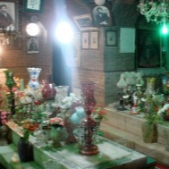 An indoor shrine with decorated graves covered in colorful vases and flowers, surrounded by framed portraits and illuminated by hanging lights.